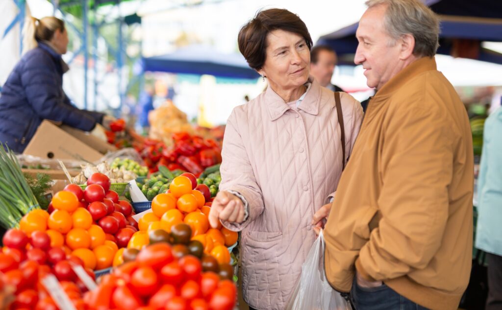 Older couple shopping at a Spanish food market, where everyday expenses are paid in euros.