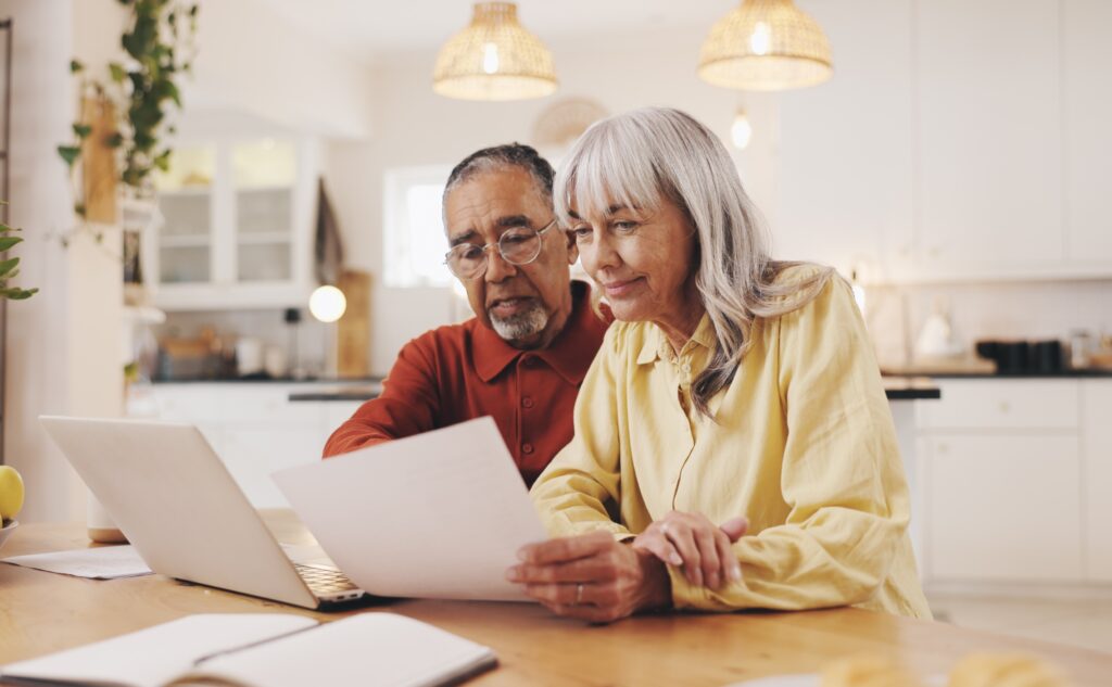 Retired couple reviewing pension paperwork and financial documents together at their kitchen table.