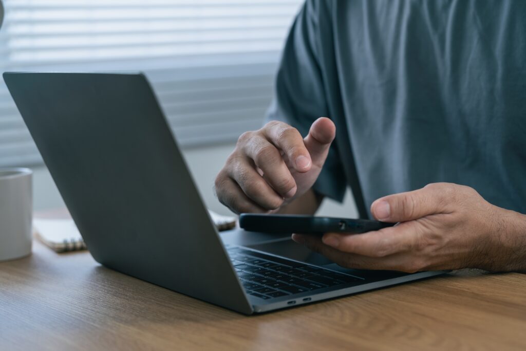 A person using a laptop and smartphone for online banking and authentication. Relevant to mistake four, about fraudulent payment instructions.
